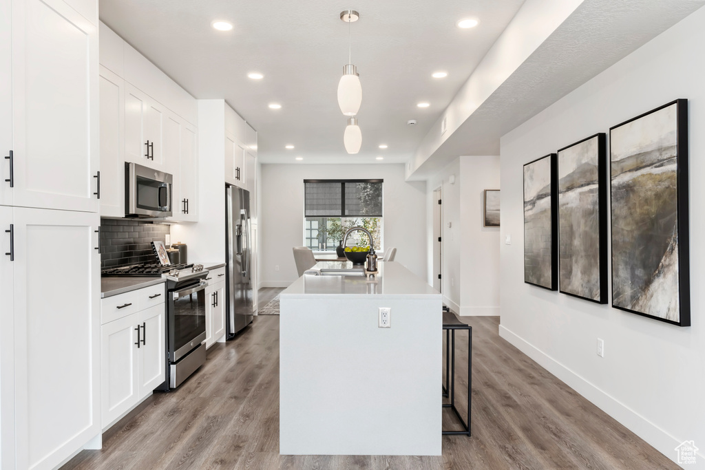 Kitchen with stainless steel appliances, a sink, a kitchen island with sink, white cabinets, and recessed lighting