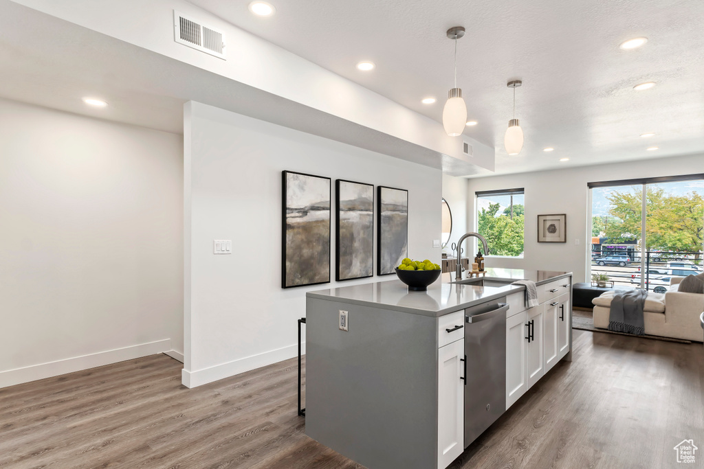 Kitchen featuring stainless steel dishwasher, open floor plan, white cabinetry, wood finished floors, and recessed lighting
