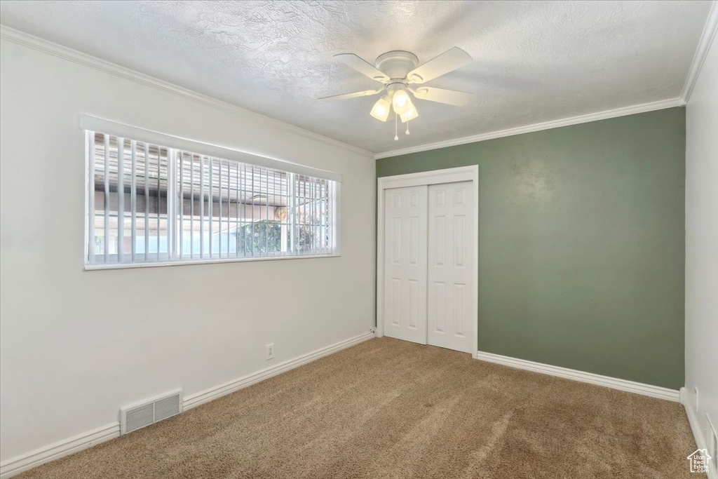 Unfurnished bedroom with carpet floors, a closet, crown molding, baseboards, and a textured ceiling