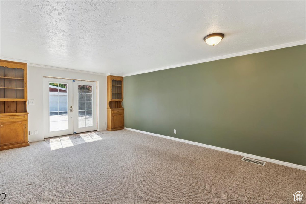 Spare room featuring french doors, carpet, ornamental molding, baseboards, and a textured ceiling