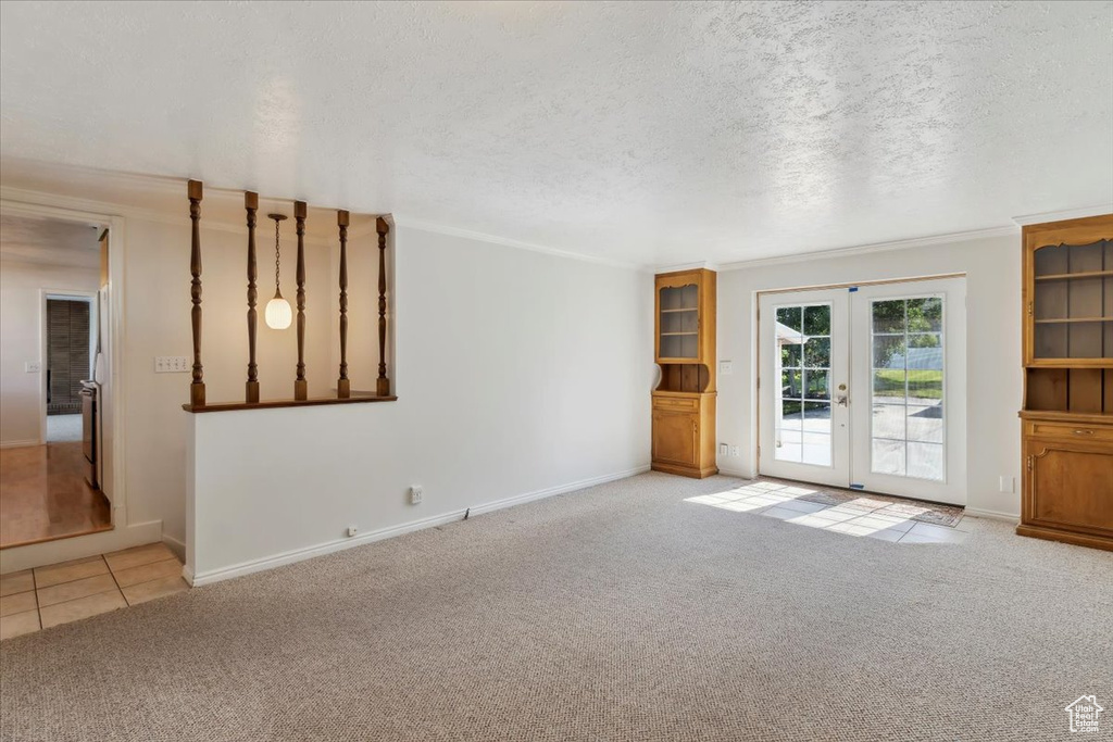 Unfurnished living room featuring carpet floors, french doors, baseboards, crown molding, and a textured ceiling