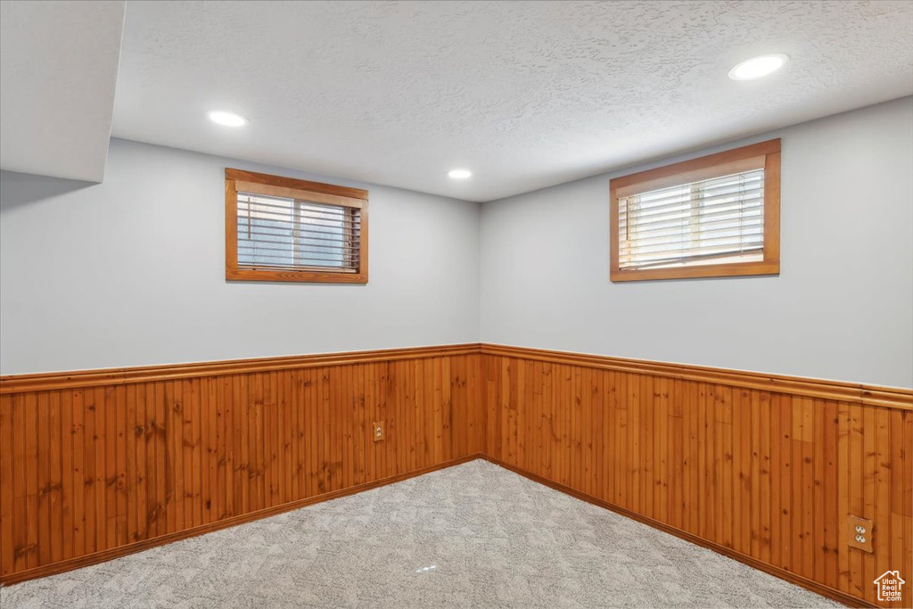 Empty room with wainscoting, a textured ceiling, wood walls, recessed lighting, and carpet