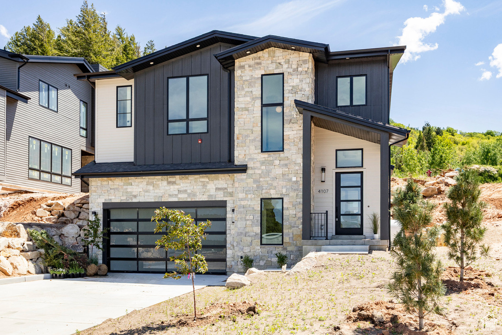 Modern home featuring board and batten siding, stone siding, an attached garage, and driveway