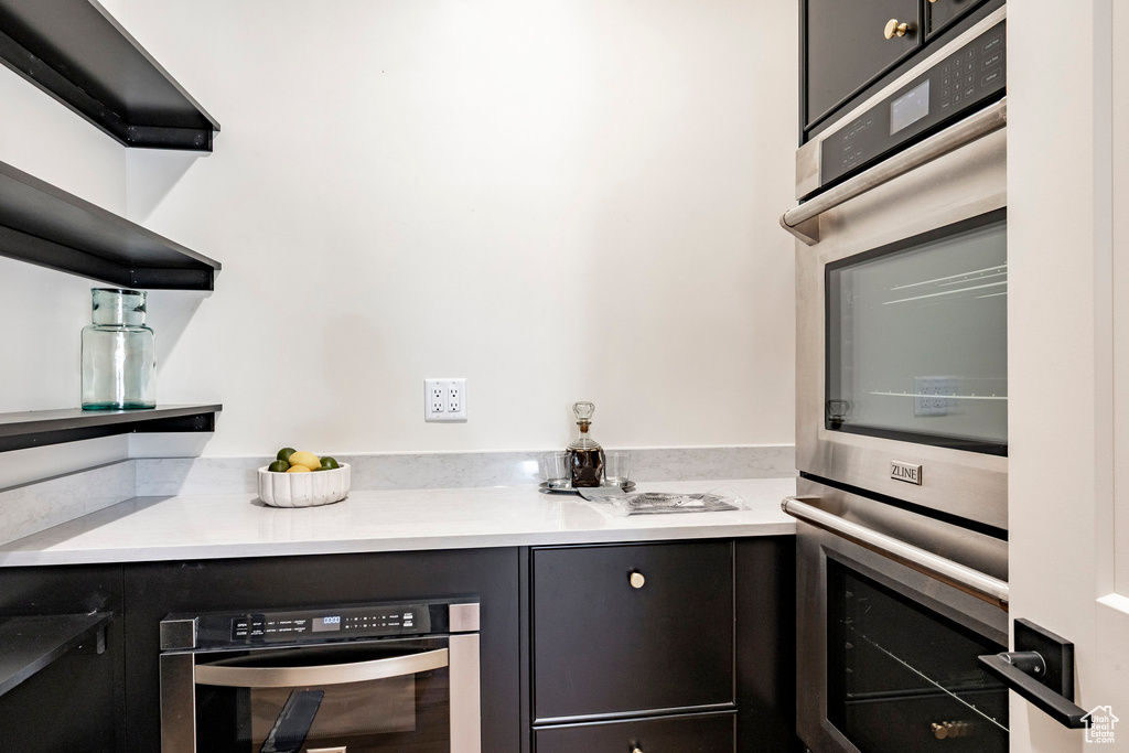 Kitchen with stainless steel double oven, open shelves, light countertops, and dark cabinetry