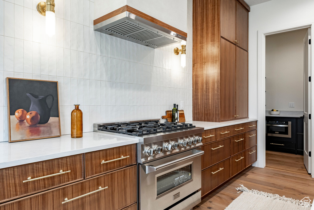 Kitchen featuring appliances with stainless steel finishes, wall chimney exhaust hood, backsplash, light countertops, and brown cabinets