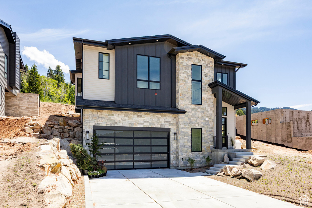 Modern home featuring stone siding, board and batten siding, driveway, and a garage