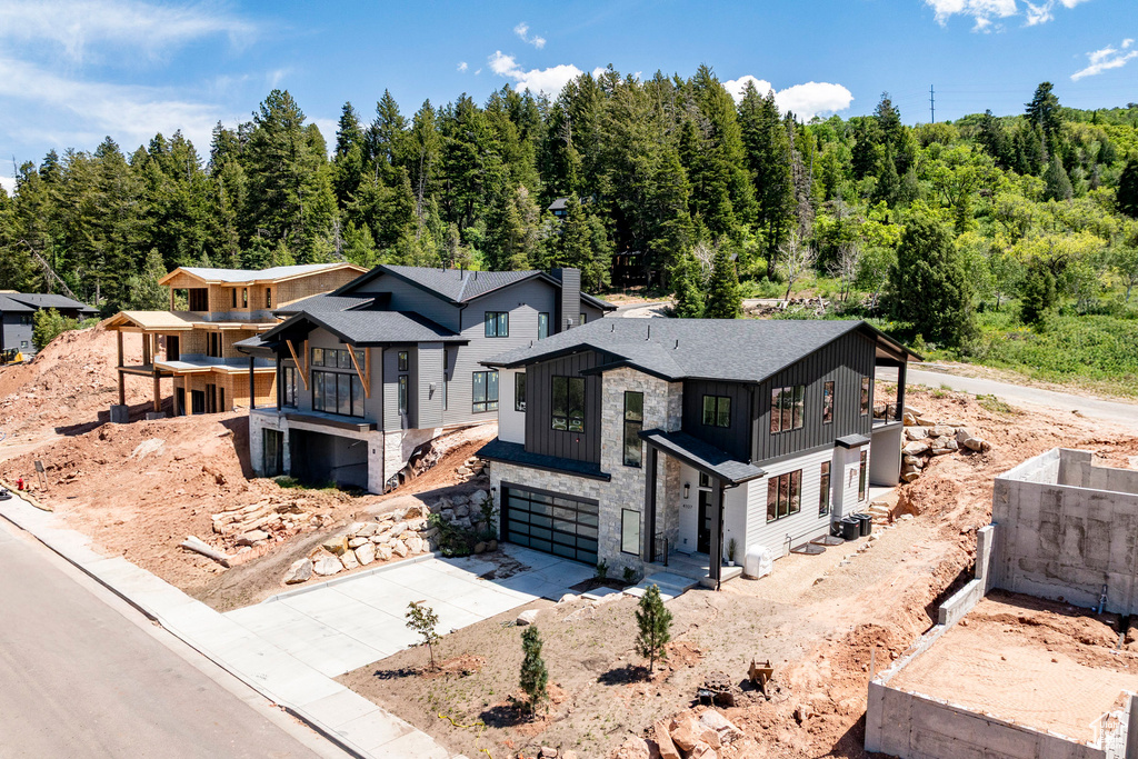 View of front of property with driveway, board and batten siding, stone siding, an attached garage, and a forest view