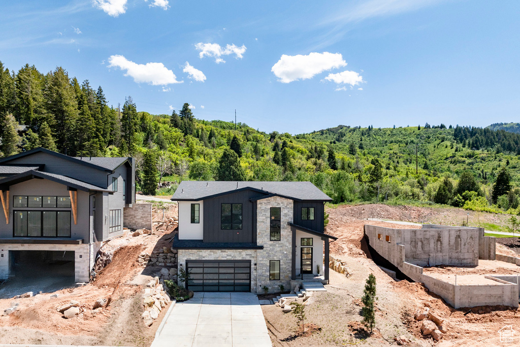 Contemporary house with a forest view, concrete driveway, a garage, and stone siding