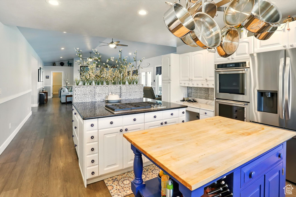 Kitchen with a center island, butcher block counters, appliances with stainless steel finishes, tasteful backsplash, and a ceiling fan