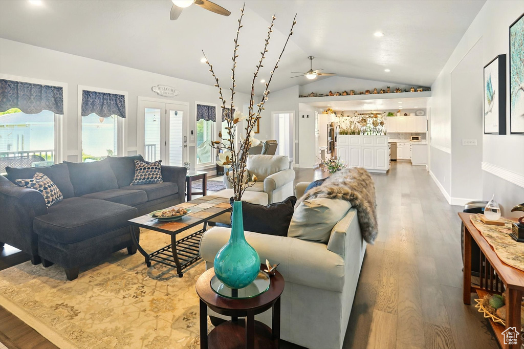 Living area with a ceiling fan, vaulted ceiling, wood finished floors, and plenty of natural light