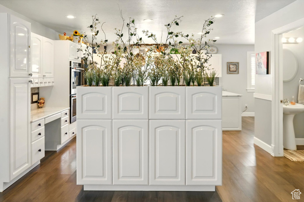 Kitchen with white cabinetry, dark wood finished floors, light countertops, stainless steel double oven, and baseboards
