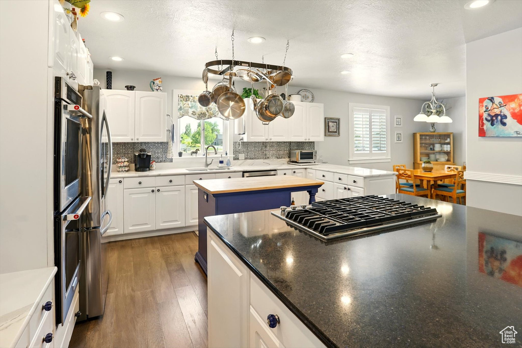 Kitchen featuring a sink, backsplash, stainless steel gas stovetop, white cabinetry, and a center island