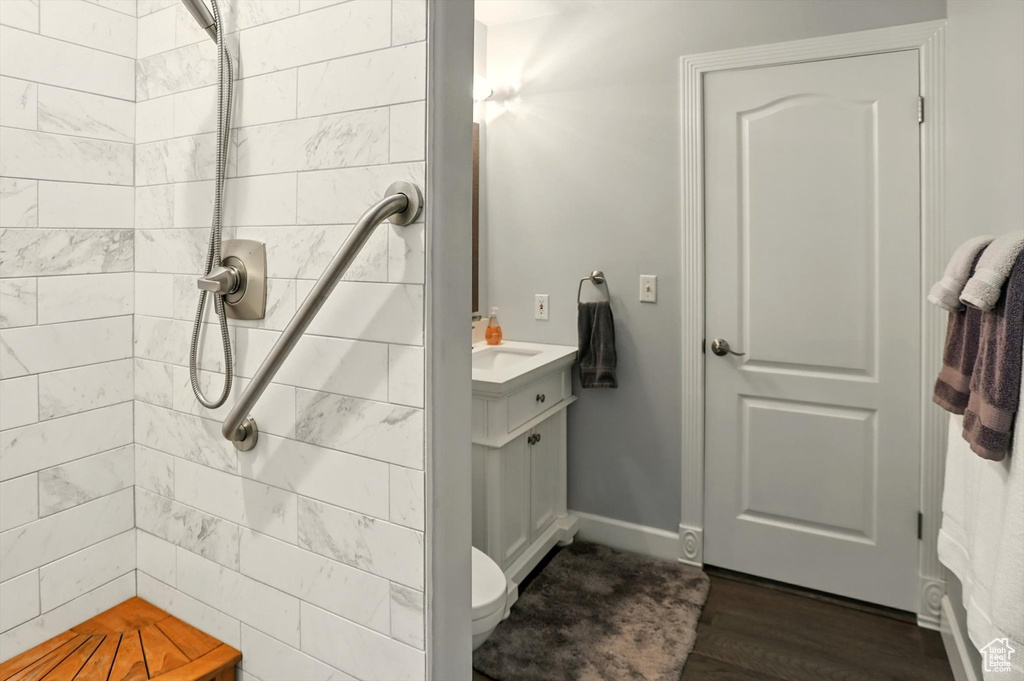 Bathroom with a tile shower, vanity, baseboards, and wood finished floors