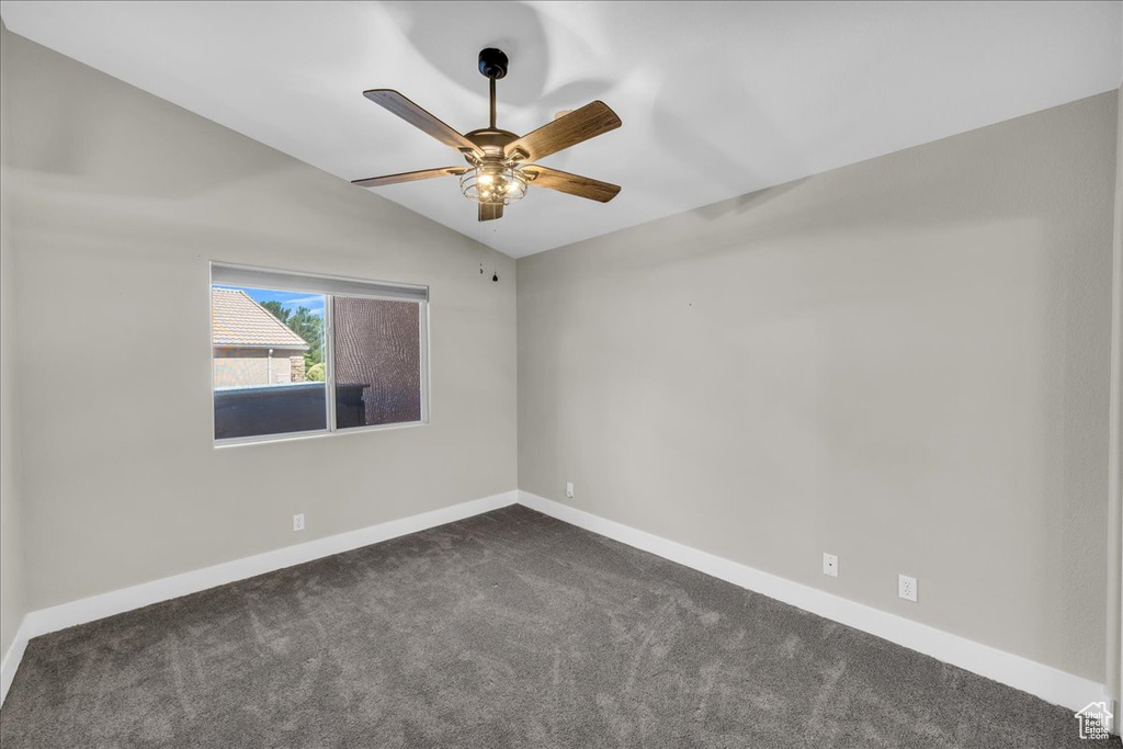 Spare room featuring a ceiling fan, vaulted ceiling, dark colored carpet, and baseboards