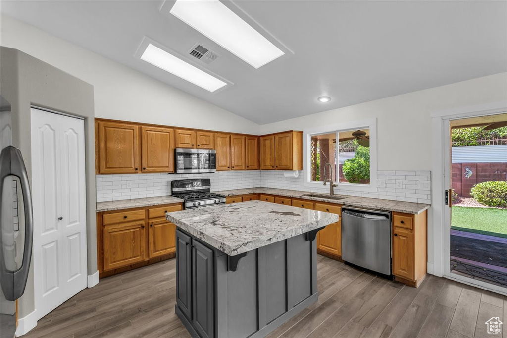 Kitchen with appliances with stainless steel finishes, a sink, lofted ceiling, a kitchen island, and wood finished floors