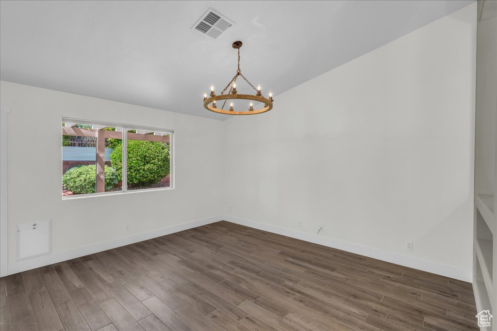 Empty room featuring a chandelier, wood finished floors, baseboards, and lofted ceiling