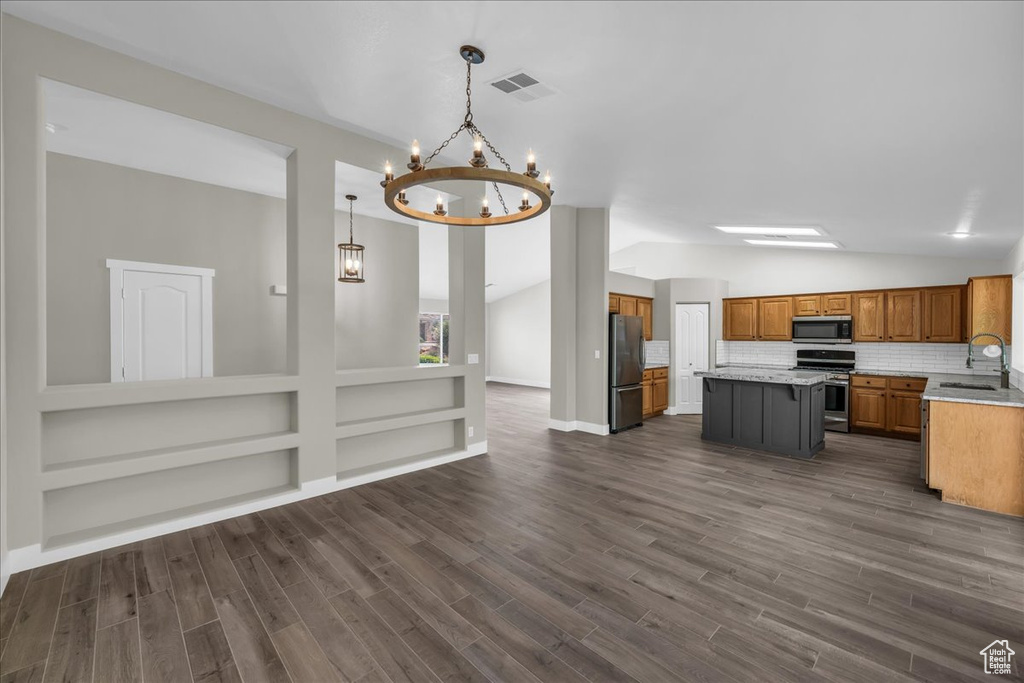 Kitchen with stainless steel appliances, lofted ceiling, brown cabinets, a chandelier, and a sink