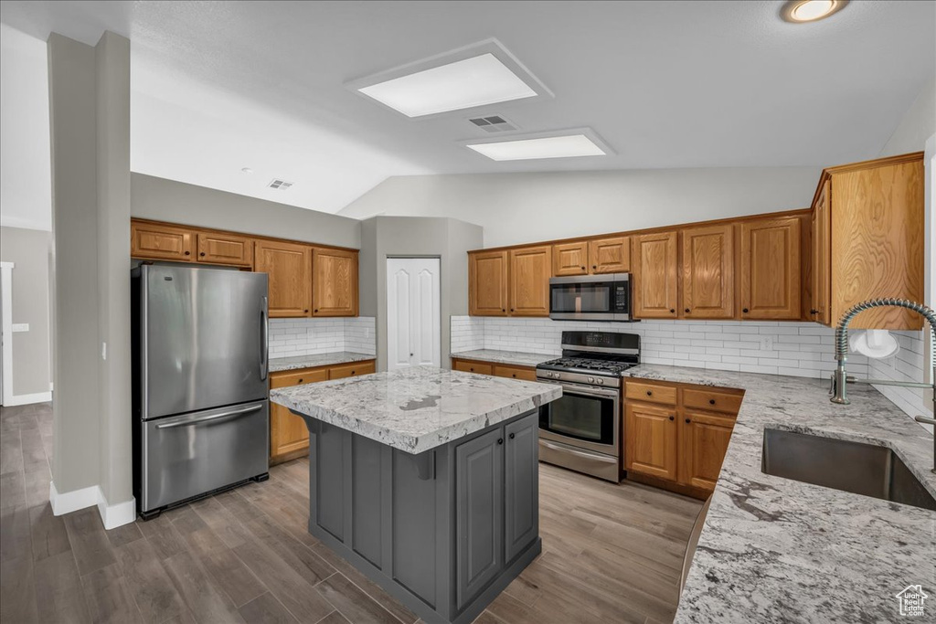 Kitchen with appliances with stainless steel finishes, a sink, a center island, vaulted ceiling, and light stone counters