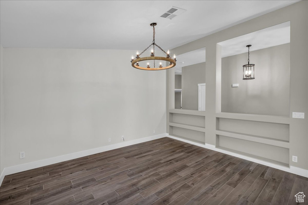 Empty room featuring a chandelier, dark wood-type flooring, baseboards, and built in features