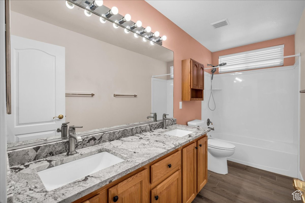 Full bathroom with toilet, double vanity, washtub / shower combination, and wood finished floors