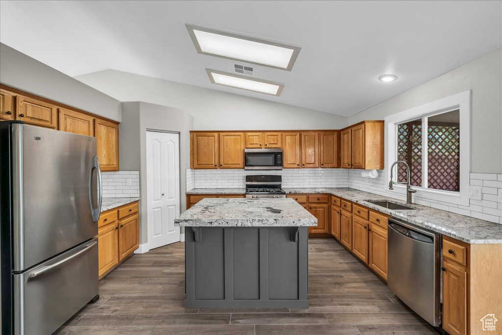 Kitchen with appliances with stainless steel finishes, a sink, lofted ceiling, a center island, and decorative backsplash