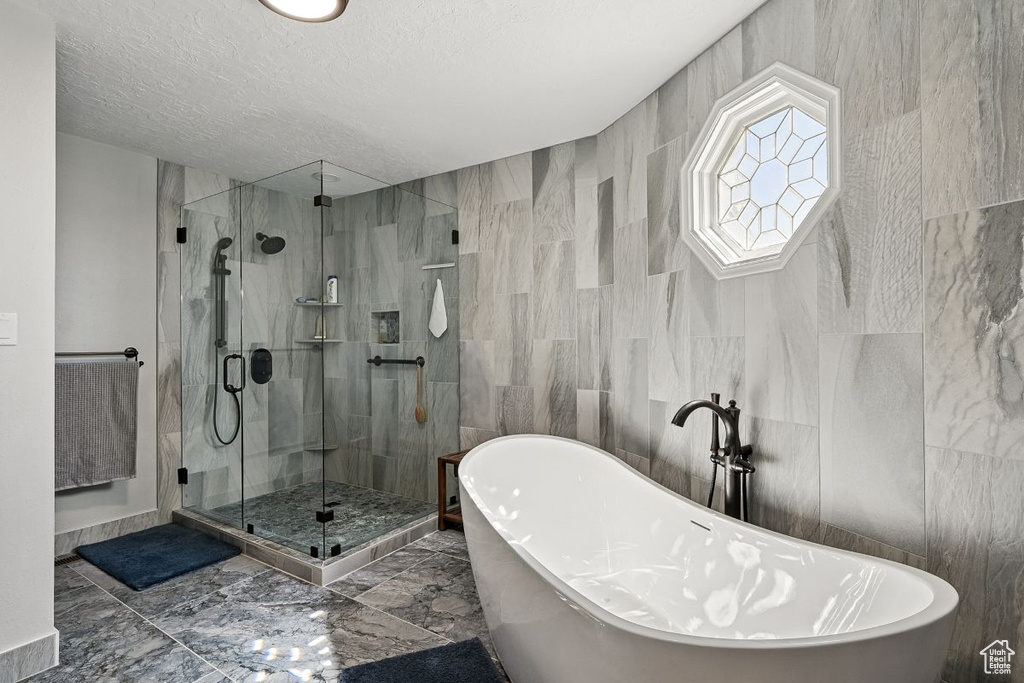 Full bath with a shower stall, a freestanding tub, marble finish flooring, a textured ceiling, and tile walls