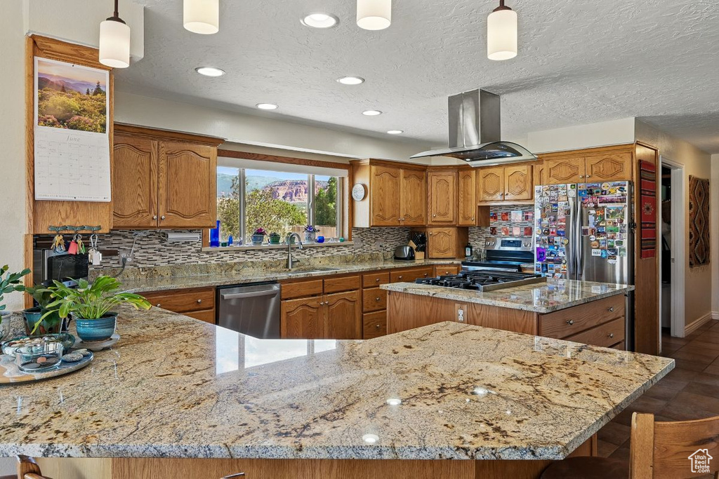 Kitchen with stainless steel appliances, island exhaust hood, brown cabinets, decorative backsplash, and recessed lighting