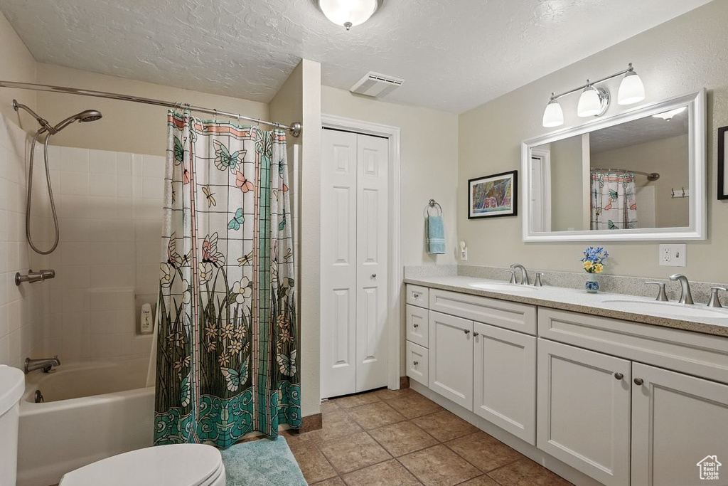 Bathroom featuring double vanity, toilet, shower / bath combination with curtain, a textured ceiling, and a closet