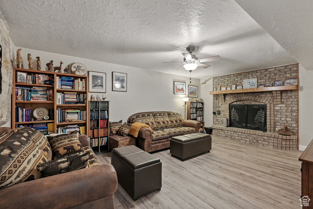 Living area with wood finished floors, a ceiling fan, a brick fireplace, and a textured ceiling