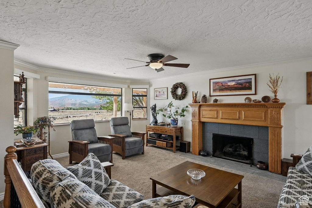 Living room featuring light colored carpet, ceiling fan, a tiled fireplace, crown molding, and baseboards