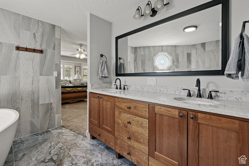 Full bath with ensuite bathroom, double vanity, a textured ceiling, marble finish flooring, and a freestanding bath