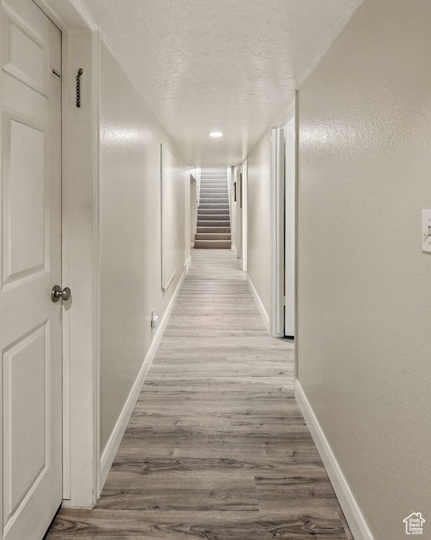 Hall featuring baseboards, wood finished floors, a textured ceiling, and stairs