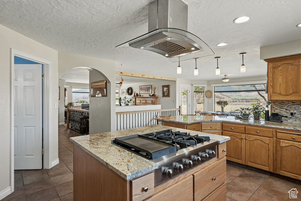 Kitchen with stainless steel gas cooktop, island range hood, a peninsula, a center island, and light stone countertops