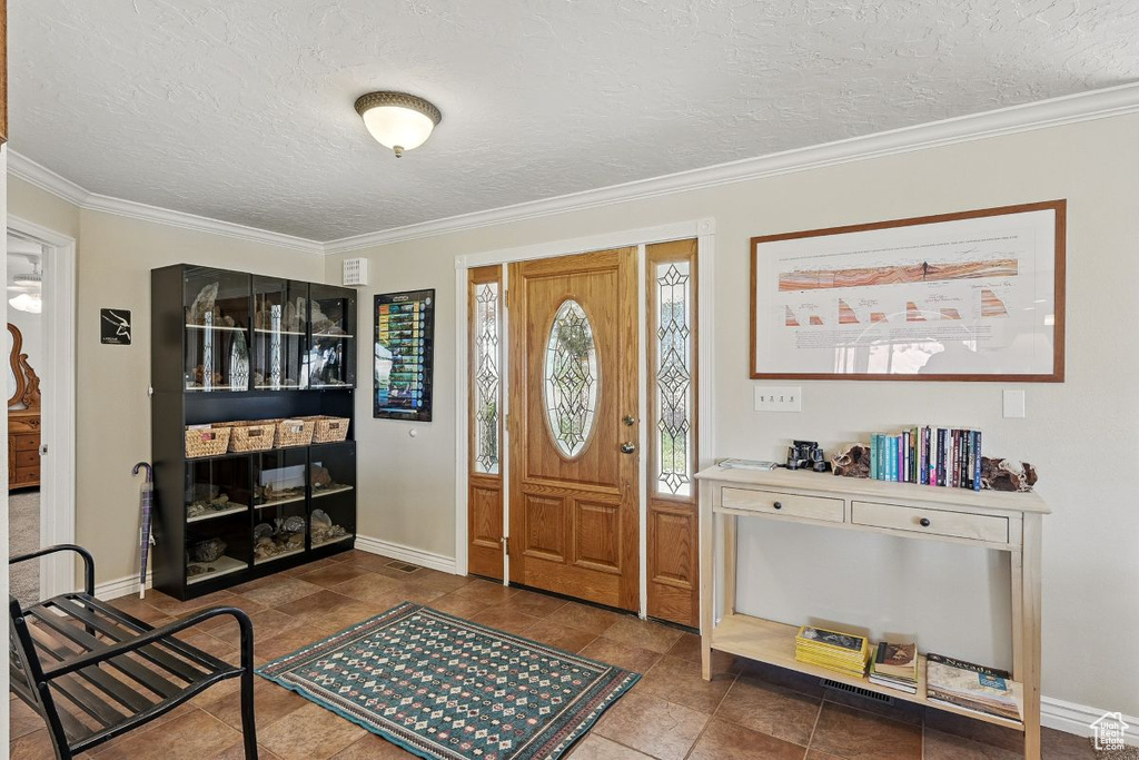 Entryway featuring a textured ceiling, ornamental molding, baseboards, and tile patterned flooring