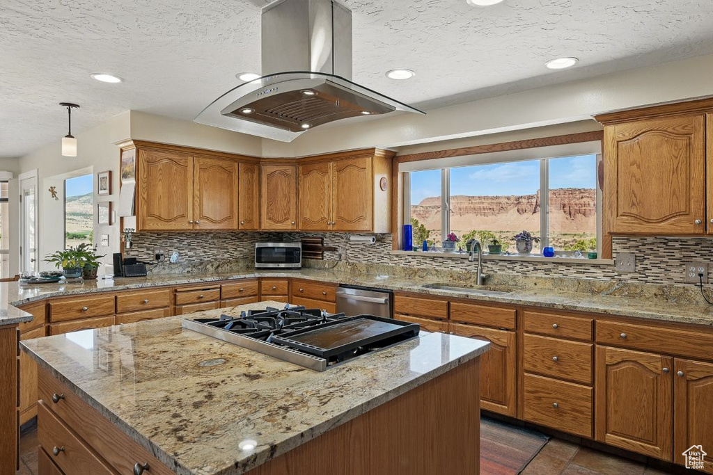 Kitchen with a sink, appliances with stainless steel finishes, island range hood, a textured ceiling, and brown cabinets