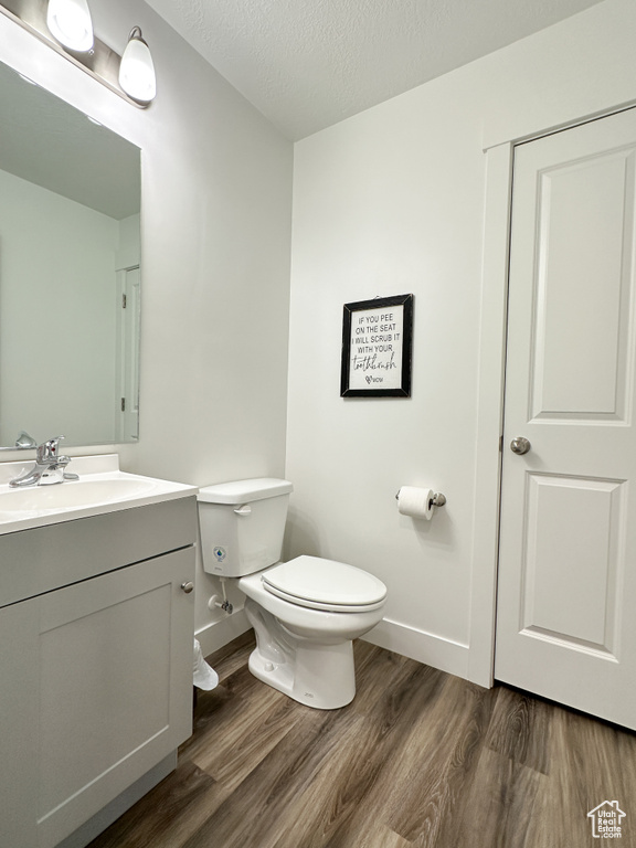 Bathroom featuring wood finished floors, toilet, vanity, a textured ceiling, and baseboards