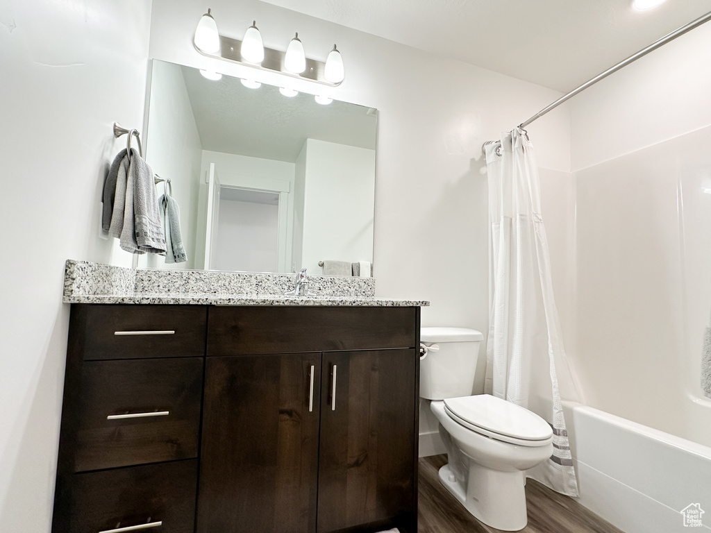 Full bathroom with toilet, vanity, wood finished floors, and shower / bath combination with curtain