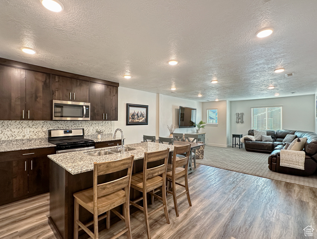 Kitchen featuring appliances with stainless steel finishes, a sink, a breakfast bar, a textured ceiling, and dark brown cabinets