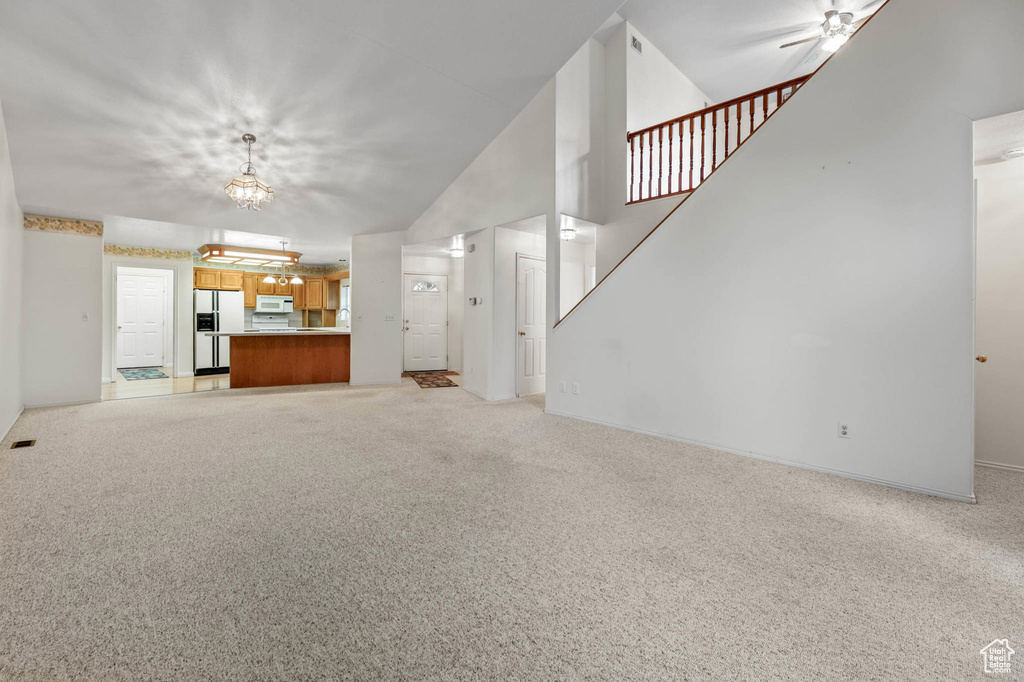 Unfurnished living room with light carpet, a chandelier, baseboards, and stairway