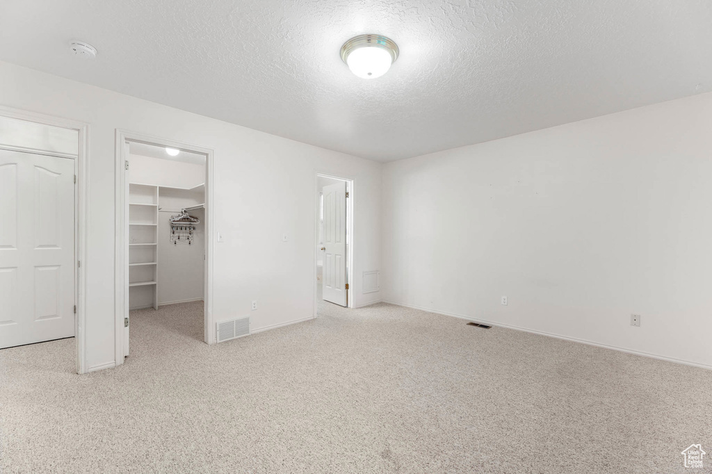 Unfurnished bedroom featuring a walk in closet, a textured ceiling, carpet, a closet, and baseboards