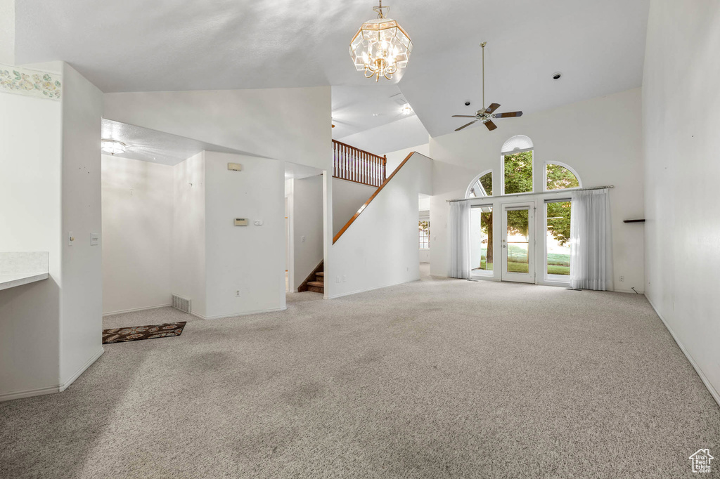 Unfurnished living room with high vaulted ceiling, carpet, stairway, a ceiling fan, and a chandelier