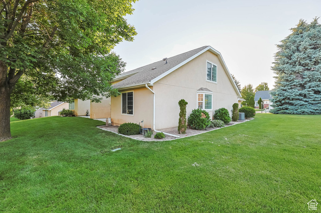 View of side of home featuring stucco siding, a yard, and central AC unit