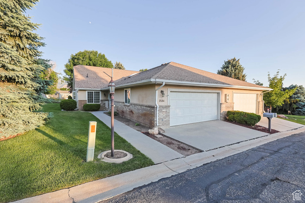 Ranch-style home featuring an attached garage, a front lawn, driveway, brick siding, and a shingled roof