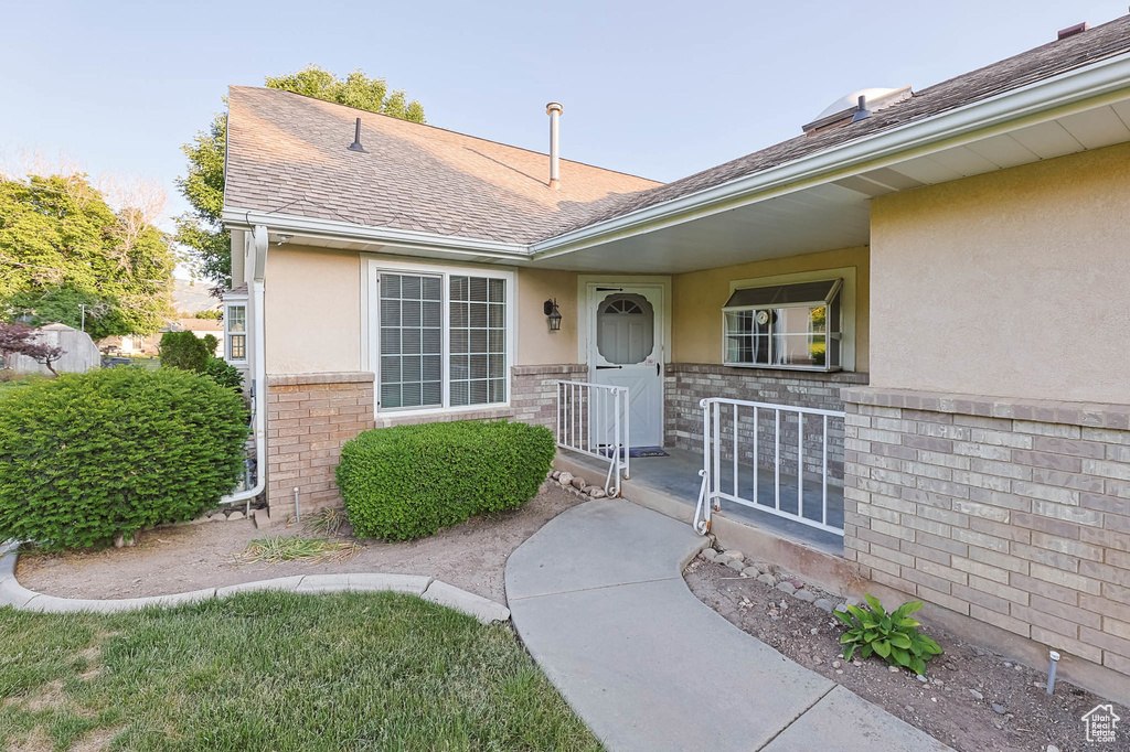 Property entrance with stucco siding, stone siding, and a shingled roof