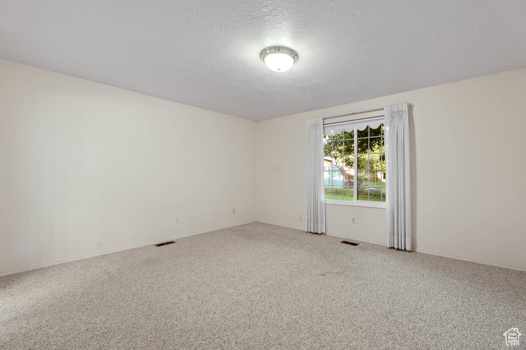 Spare room with a textured ceiling, light colored carpet, and baseboards