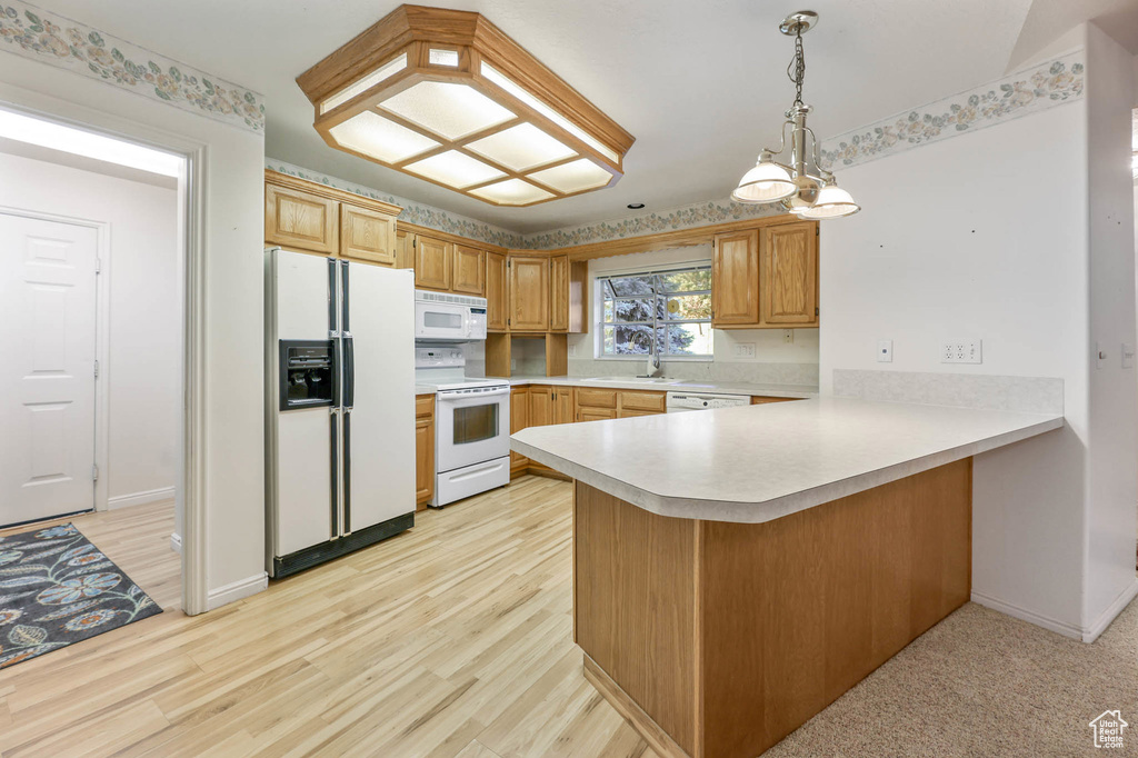 Kitchen with white appliances, light countertops, a peninsula, light wood-style flooring, and a sink