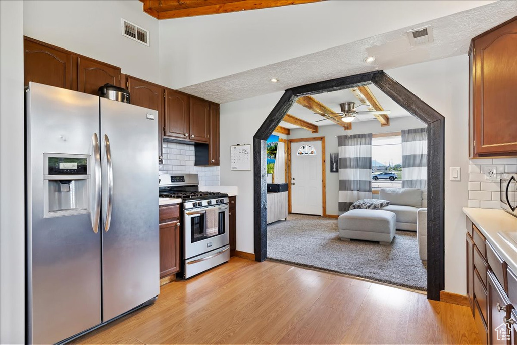 Kitchen featuring stainless steel appliances, ceiling fan, light wood-style floors, backsplash, and beamed ceiling