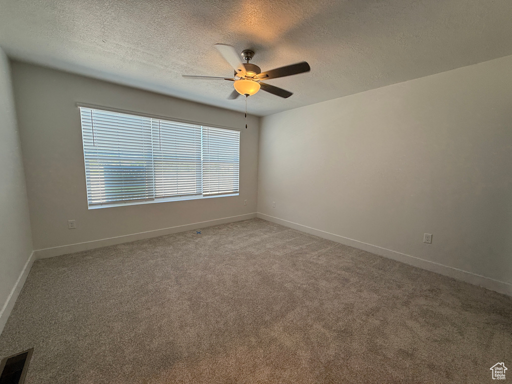 Empty room with ceiling fan, a textured ceiling, light carpet, and baseboards