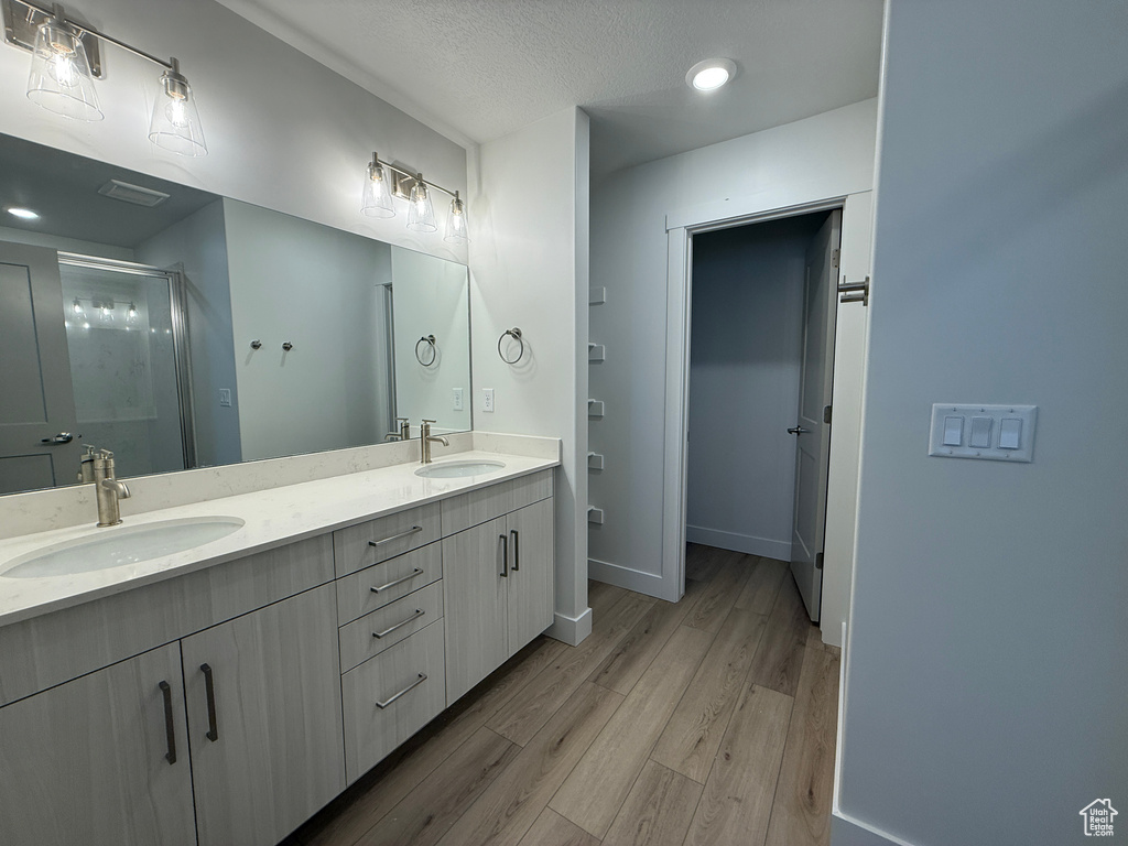 Bathroom with wood finished floors, double vanity, a shower stall, baseboards, and recessed lighting