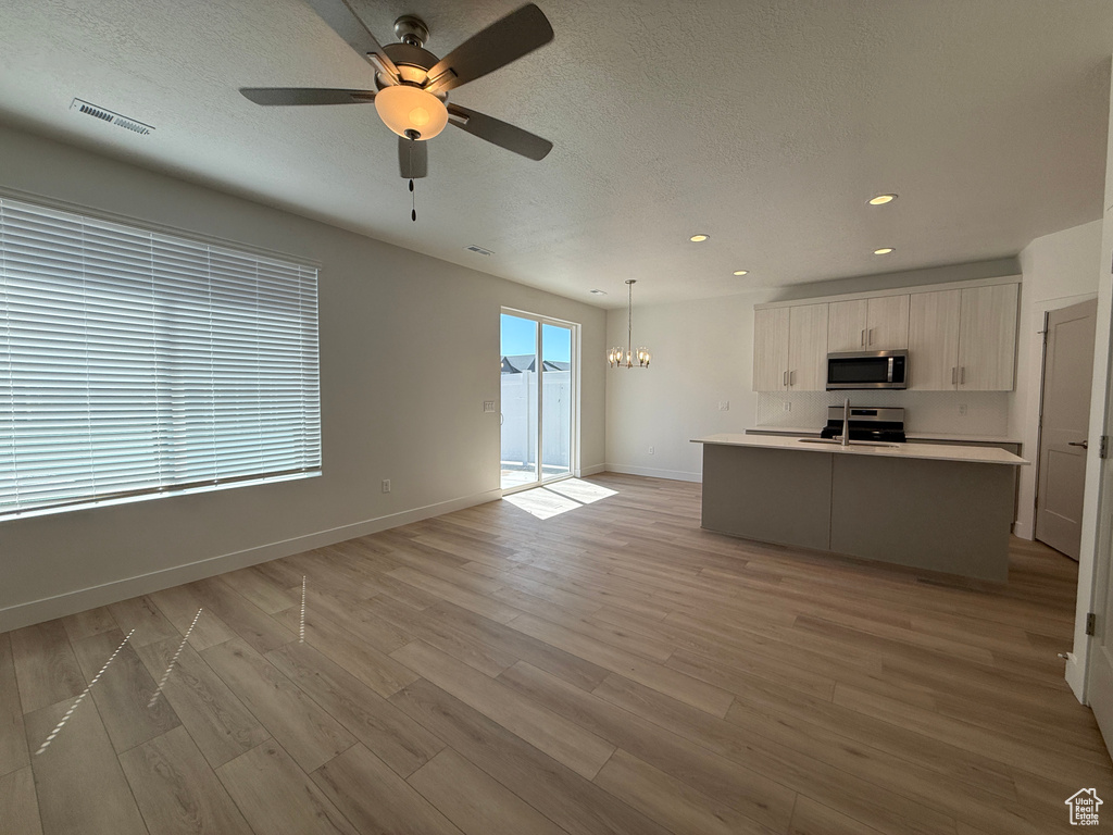 Unfurnished living room featuring ceiling fan, light wood-type flooring, baseboards, recessed lighting, and a chandelier